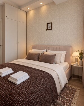 Een netjes opgemaakt bed met een bruin-wit gebeddeken, een nachtkastje met een lamp en een klein, ingelijst foto op de muur.