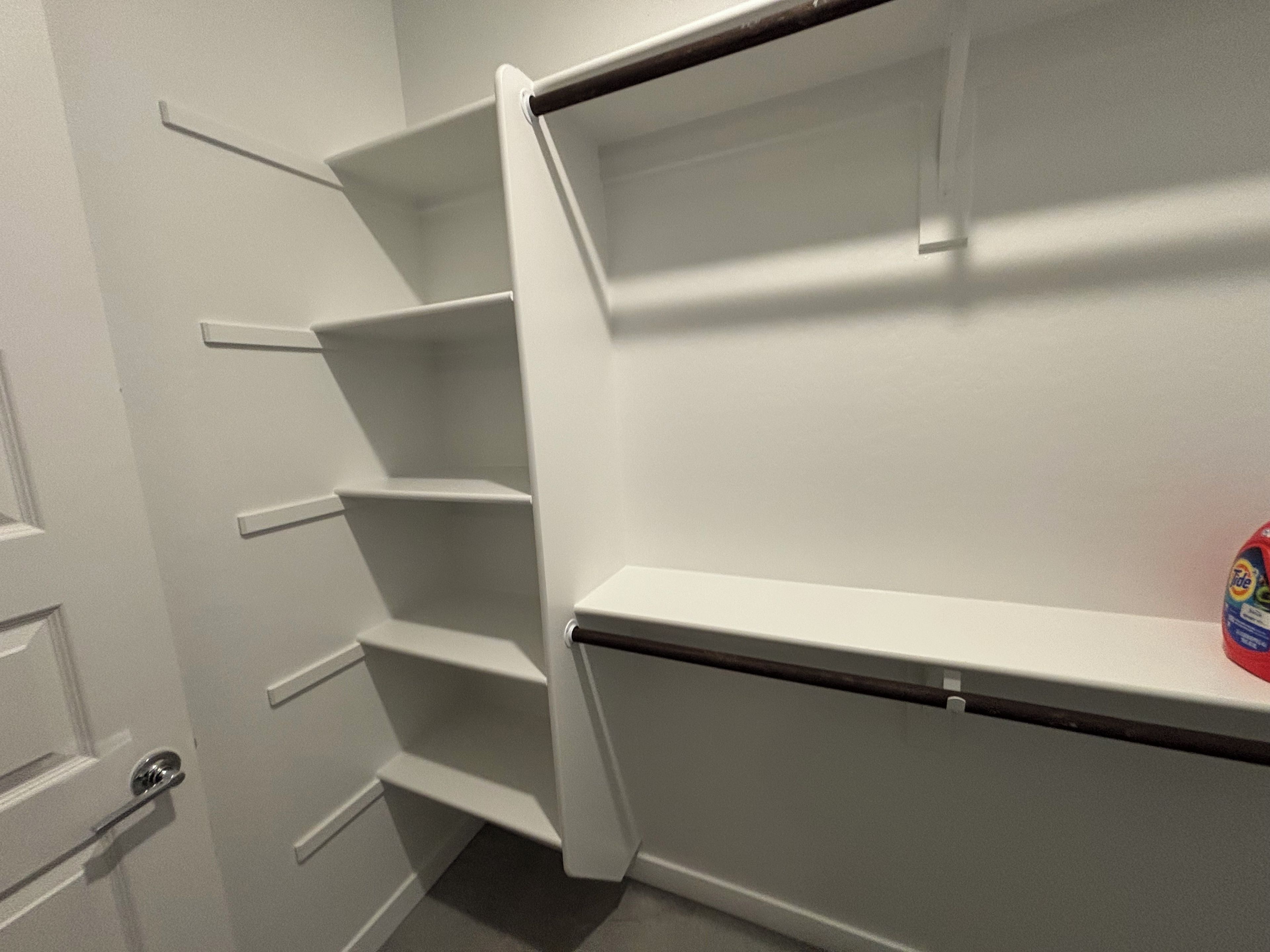 A white interior space with a door, a shelf unit, and a box of Tide laundry detergent.