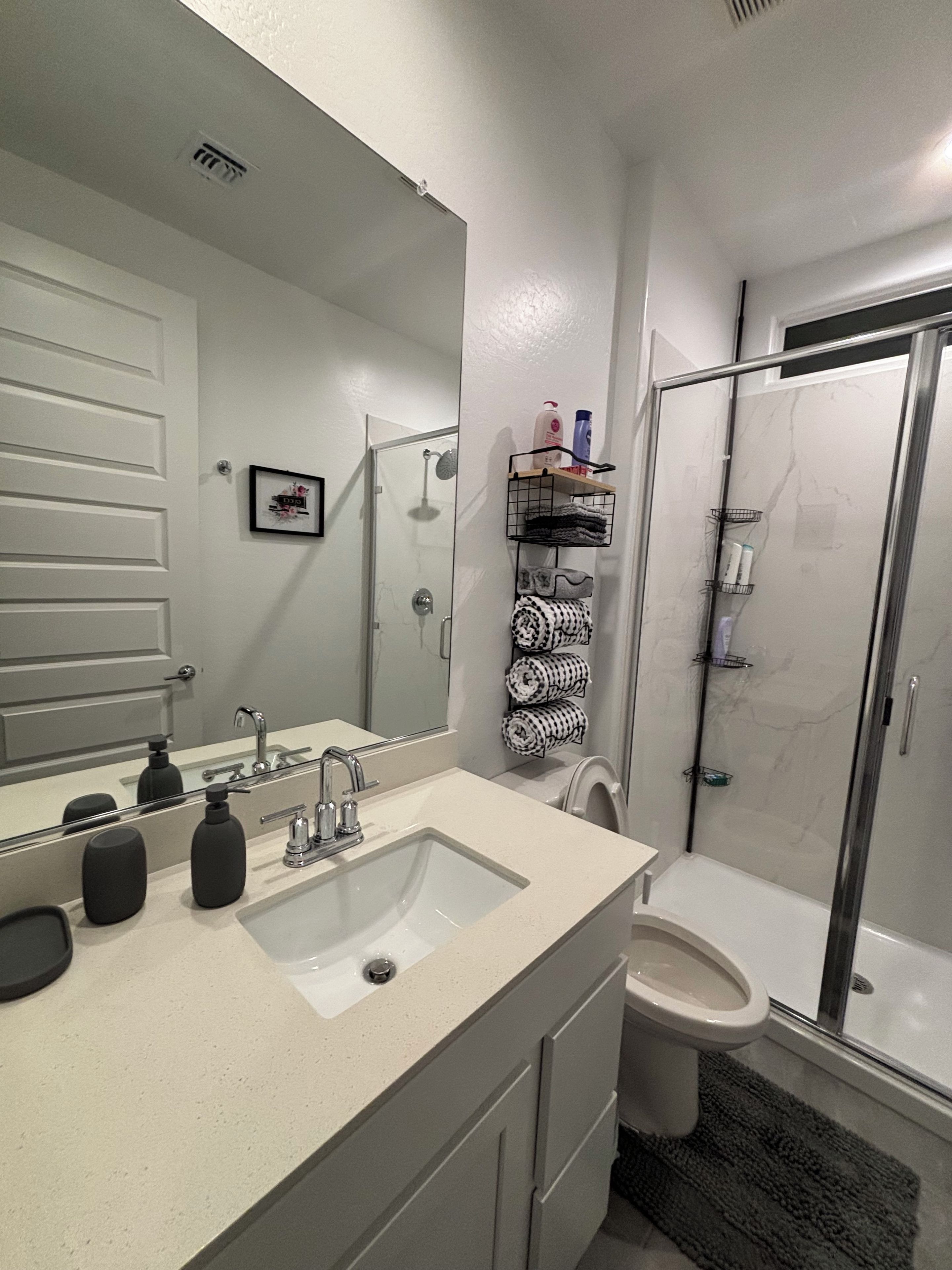 A bathroom with a sink, mirror, toilet, and shower.