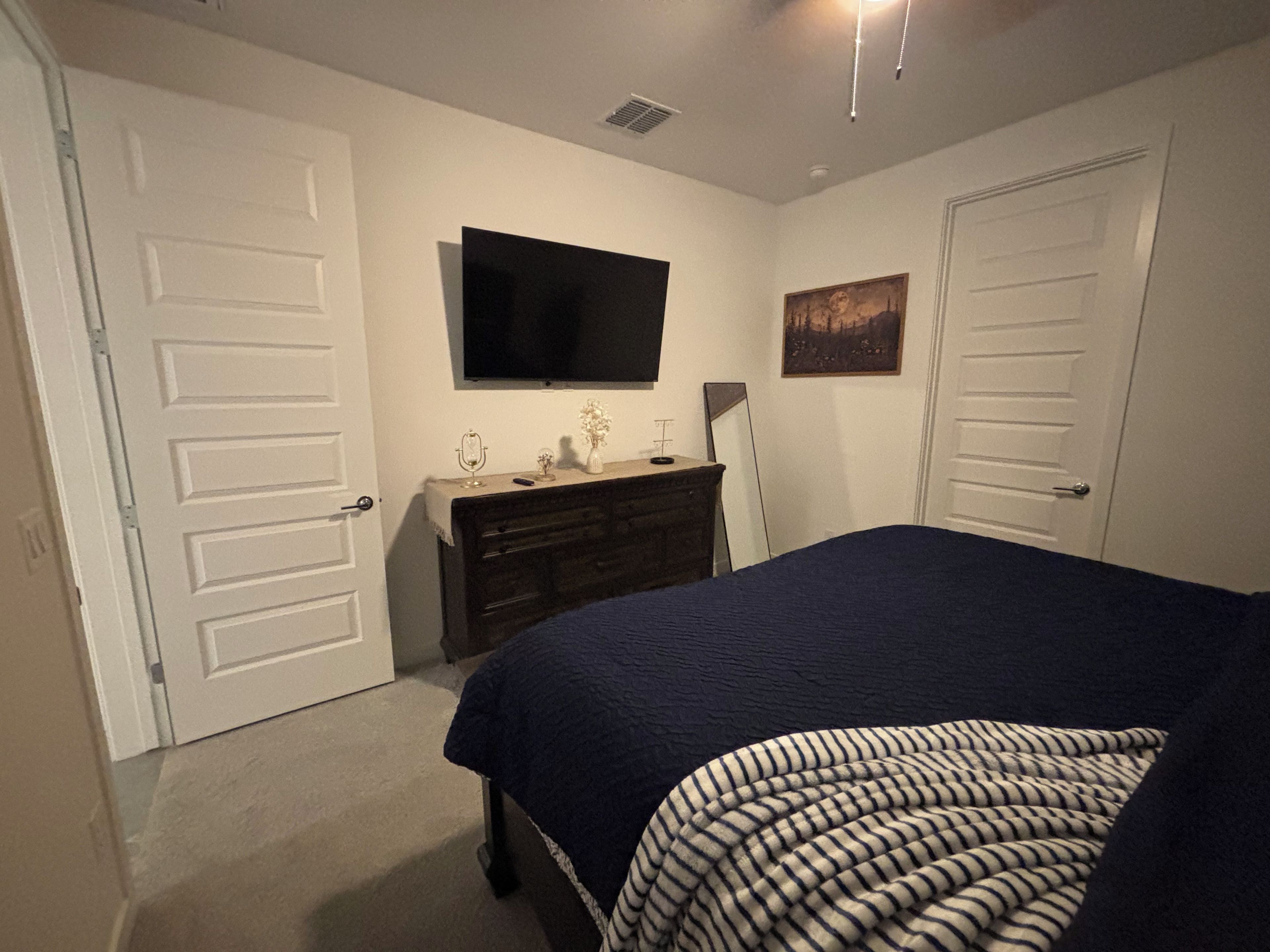 A bedroom with a bed, dresser, television, and doors.