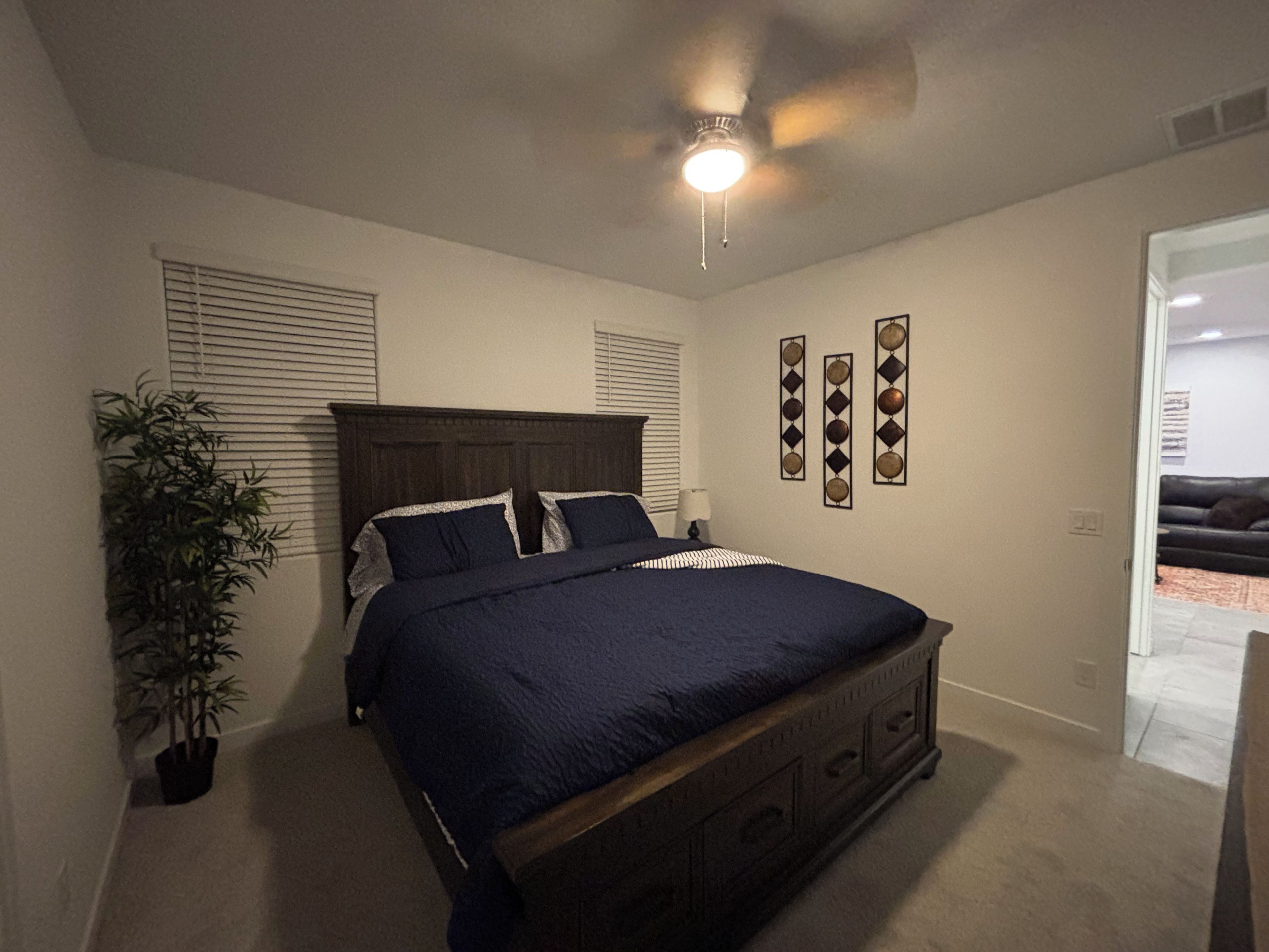 A bedroom with a bed, a ceiling fan, a potted plant, and decorative wall art.