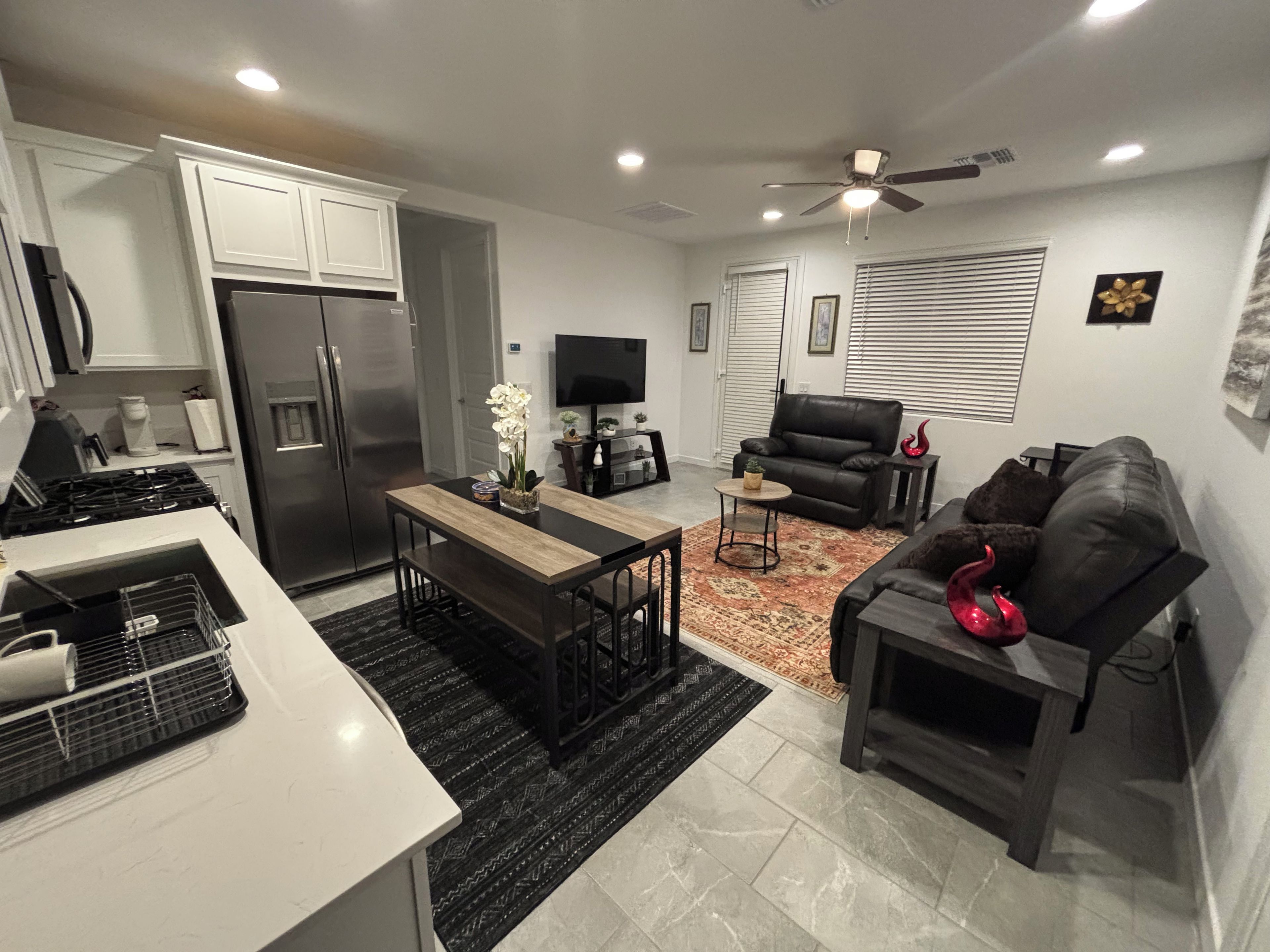 A modern kitchen with a refrigerator, stove, and dining area. There is a living room with a sofa, a coffee table, and a TV.