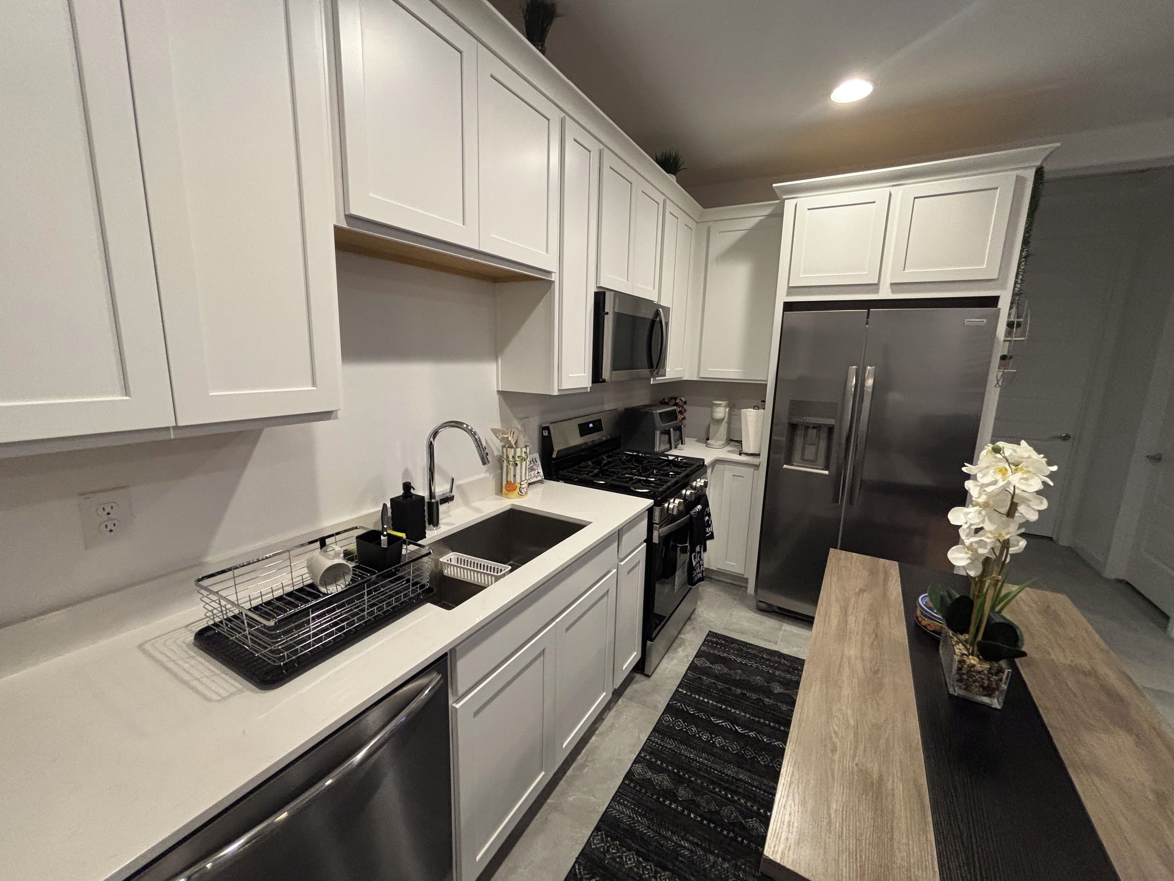 Una cocina moderna con armarios blancos, electrodomésticos de acero inoxidable y una mesa de comedor de madera.