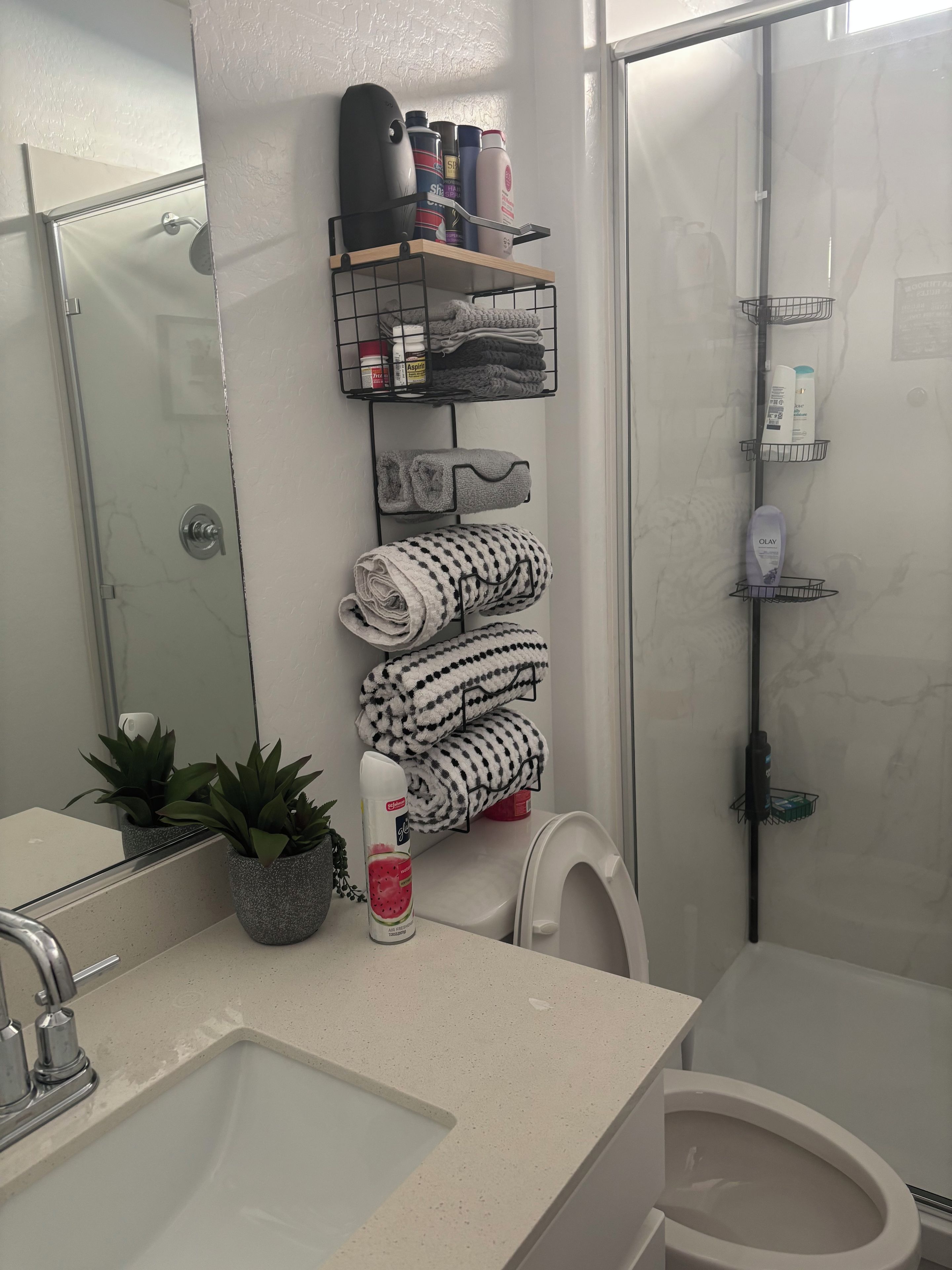A bathroom with a glass shower enclosure, a toilet, a sink with a mirror, and towel racks with folded towels and toiletries.