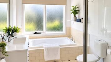 A modern bathroom with a large bathtub, a glass shower enclosure, and a window with frosted glass.