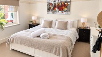 A bedroom with a bed, two bedside tables, a wall-mounted painting, and a window with a view of a brick building.