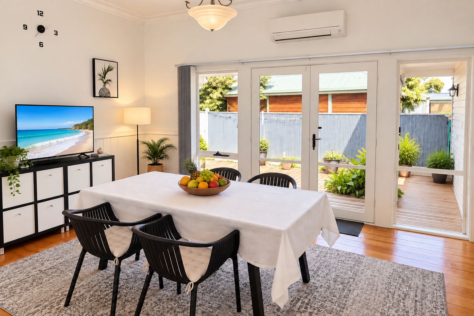 A dining area with a table set for two, a fruit bowl on the table, and a television on a cabinet.