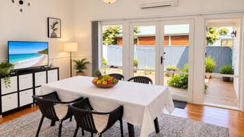 A dining area with a table set for two, a fruit bowl on the table, and a television on a cabinet.