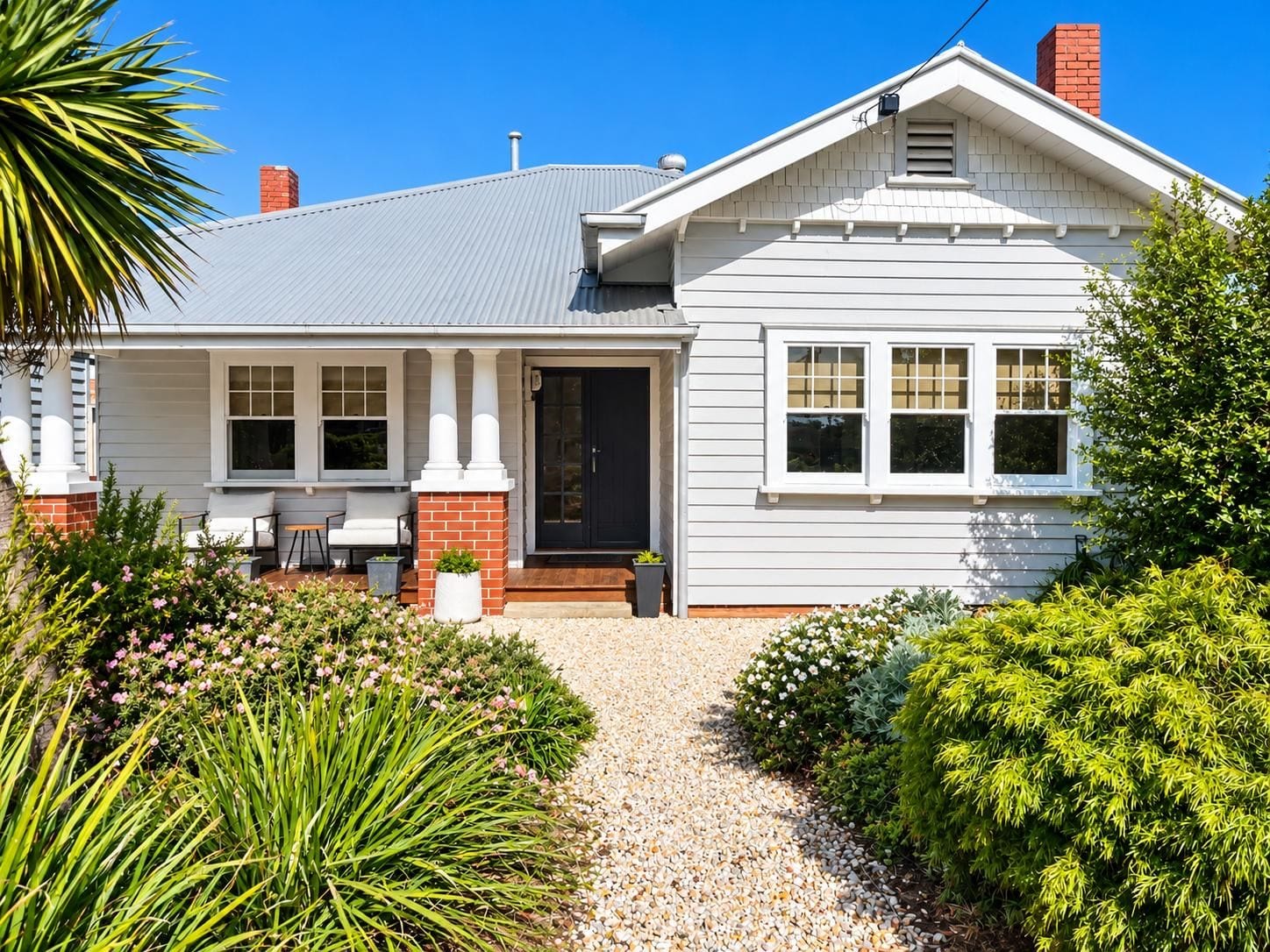 A two-story house with a front porch, a brick chimney, and a gravel driveway.