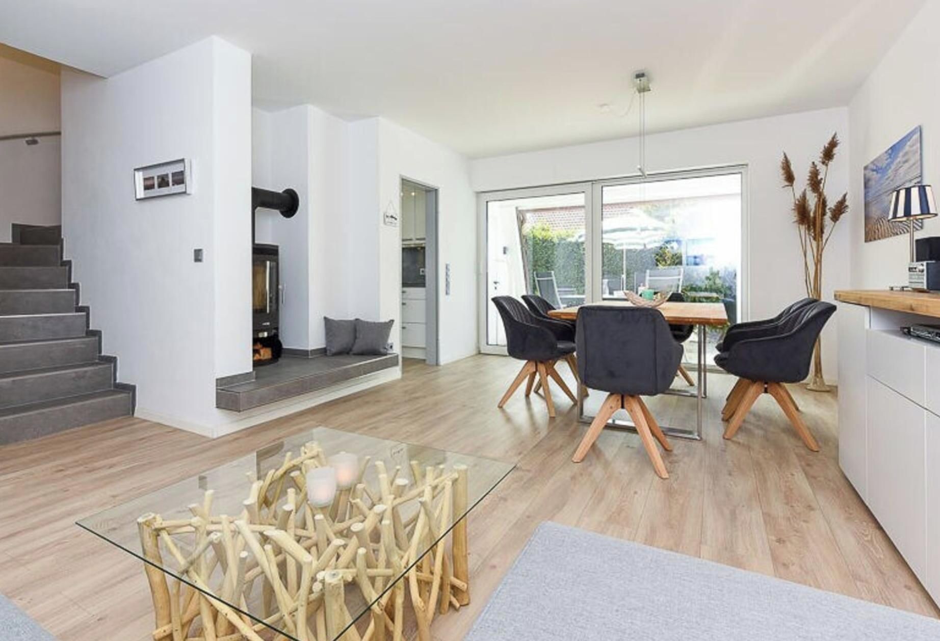 Espaço de estar moderno com escada, área de jantar com cadeiras, mesa de centro de vidro e cozinha.