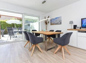 A modern dining area with a wooden table and chairs, a glass door leading outside, and a television on a wooden counter. - Fries at the Marina (Wittmund)