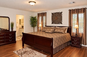 A bedroom with a wooden bed, bedside tables, a mirror, a decorative wall piece, and a potted plant. - Spacious 4-bedroom house in peaceful Houston with Fenced Yard! (Houston)