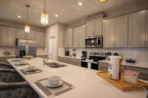 Cozinha moderna com eletrodomésticos de aço inoxidável, uma ilha central e iluminação pendente.