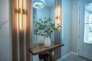 A hallway with a wooden console table, two white vases with plants, and a modern light fixture. - Luxury 9BR Home Near Disney | Solara Resort 81SA (Kissimmee)