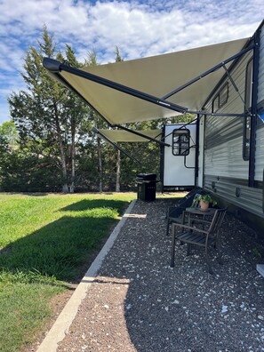 Un espace extérieur abrité, équipé d’un barbecue, de sièges et d’une plante en pot.