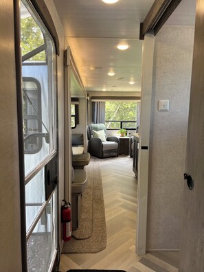 Ein schmaler Gang, der in einen Sitzbereich mit einem Feuerlöscher, einem Fenster und einer Tür führt.