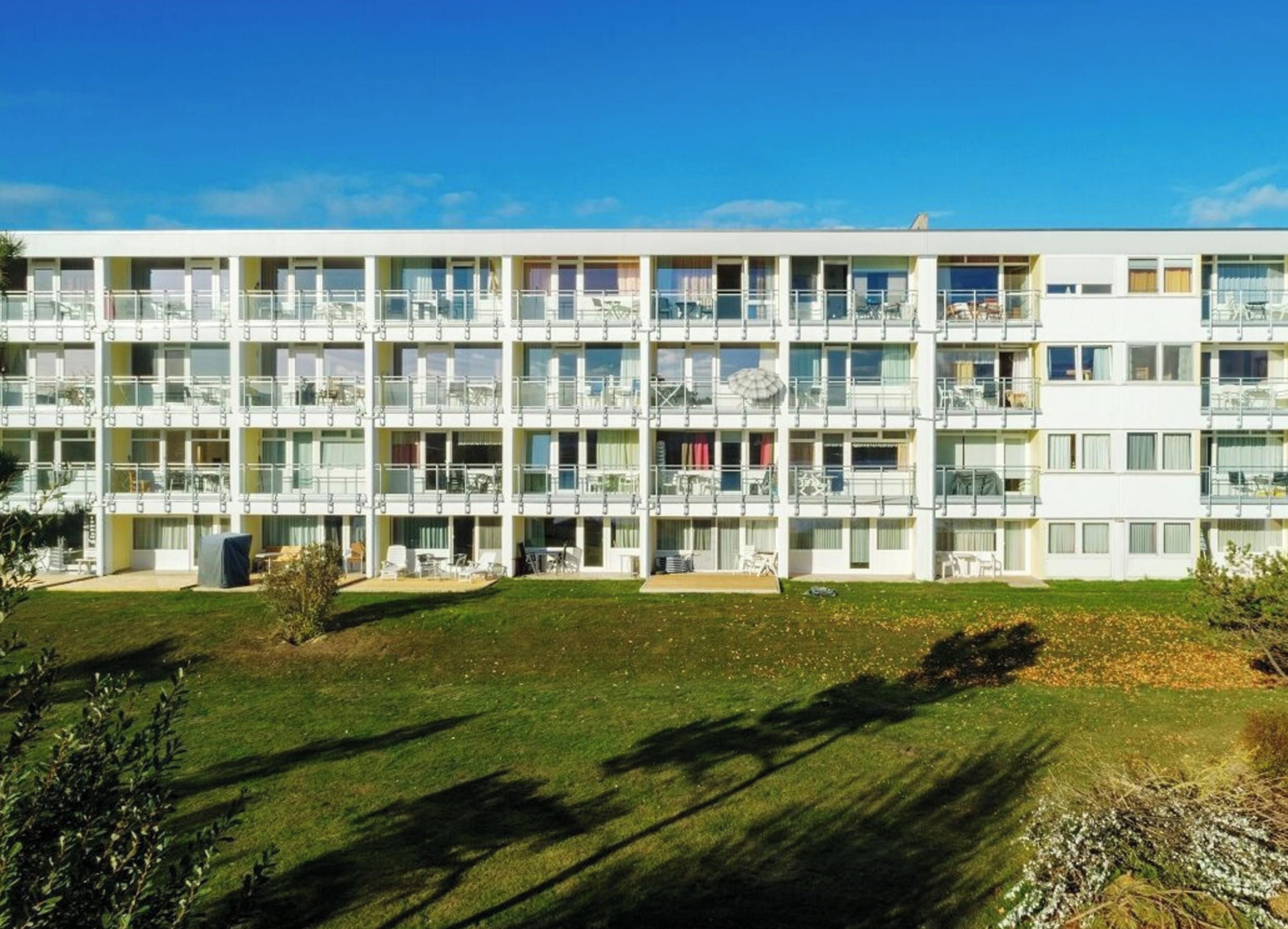 A multi-story hotel building with balconies, outdoor seating, and a well-maintained lawn.