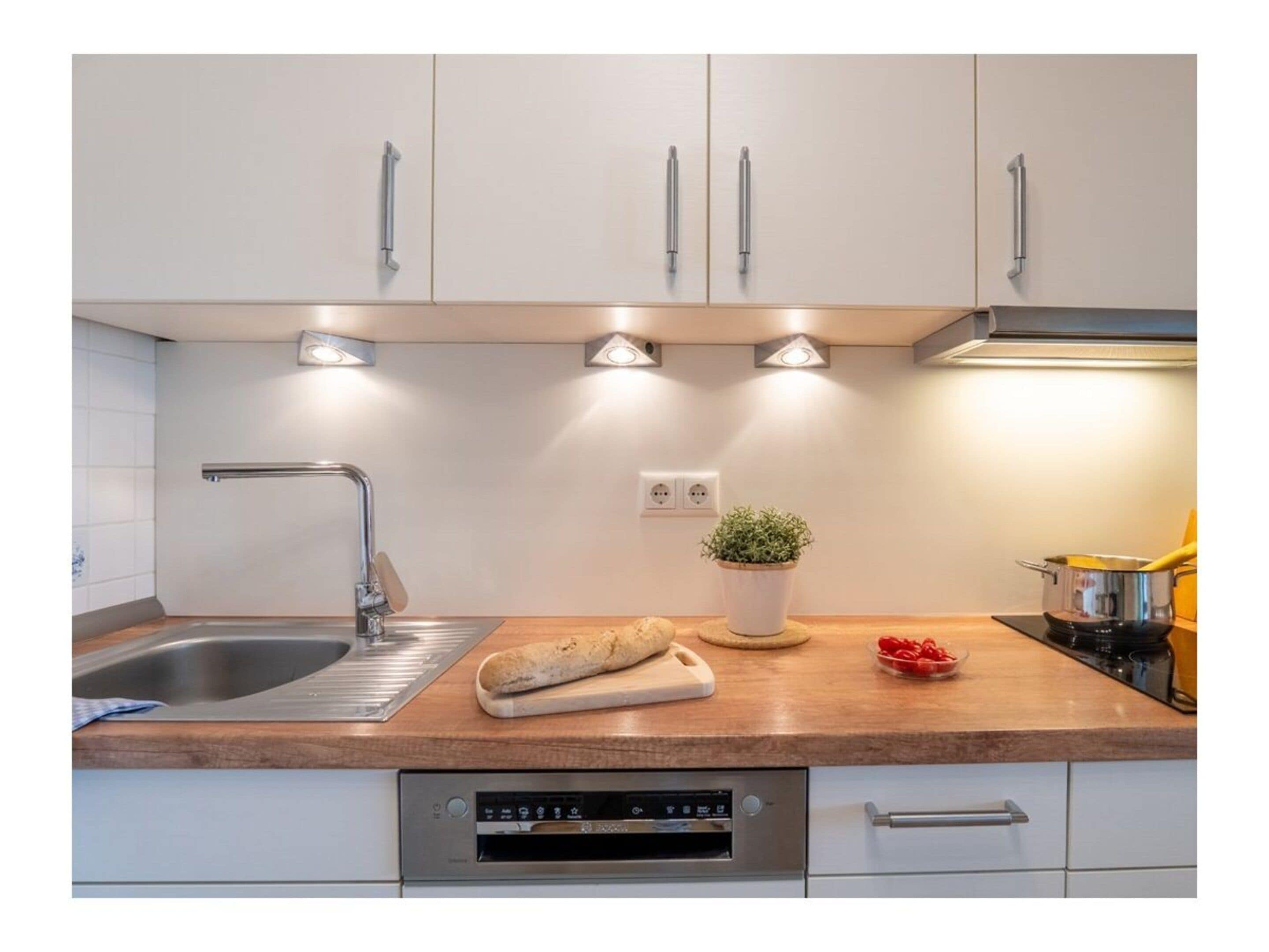 Eine moderne Küche mit Edelstahlspüle, eingebautem Backofen und einer Arbeitsplatte mit Topfpflanze und Brot.