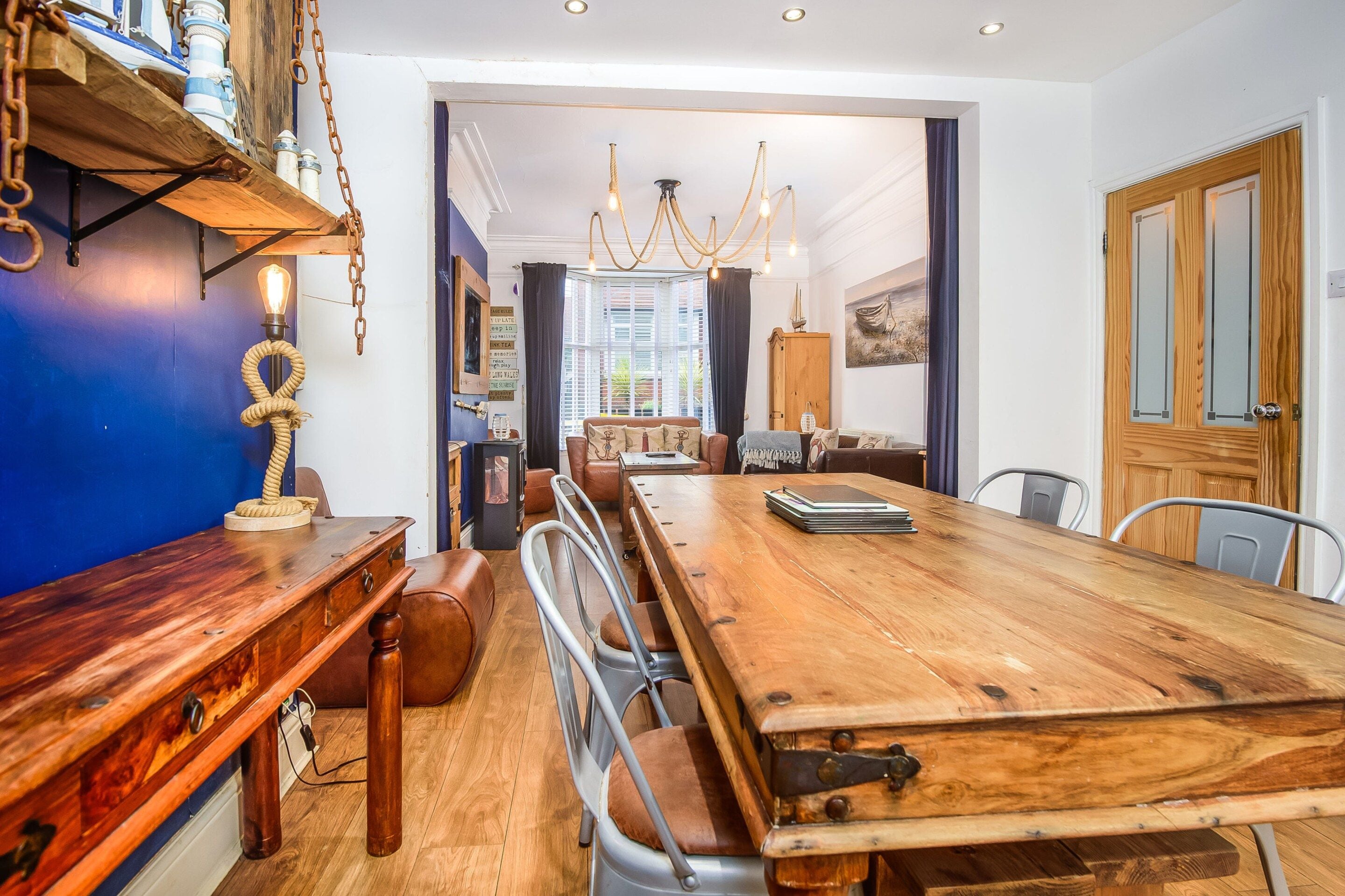 A spacious dining area with a long wooden table, metal chairs, and a chandelier.