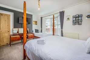 Ein Hotelzimmer mit Himmelbett, Schreibtisch mit Stuhl, Fernseher und Fenster mit Jalousien.