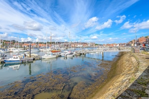 Ein Hafen mit vertäuten Booten, eine Uferpromenade und Gebäude im Hintergrund.