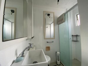 A bathroom with a white sink, a mirror, a glass shower enclosure, and a toilet. - Vrbo Property (Balneário Camboriú)