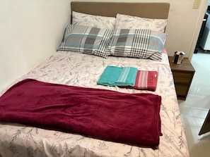 A bed with floral bedding, two pillows, a red blanket, and a folded towel. - Vrbo Property (Balneário Camboriú)