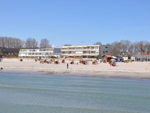 A beachside building with multiple balconies, a sandy beach in the foreground, and a clear sky. - Holiday Apartment With 1 Bedroom (Grossenbrode)