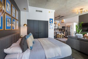 Ein modernes Schlafzimmer mit einem großen Bett, einer Couch und einem durch eine offene Tür einsehbaren Küchenbereich.