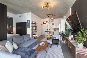 Ein modernes Wohnzimmer mit grauem Sofa, Couchtisch aus Holz und einem Essbereich, im Hintergrund ist eine Küche zu sehen.