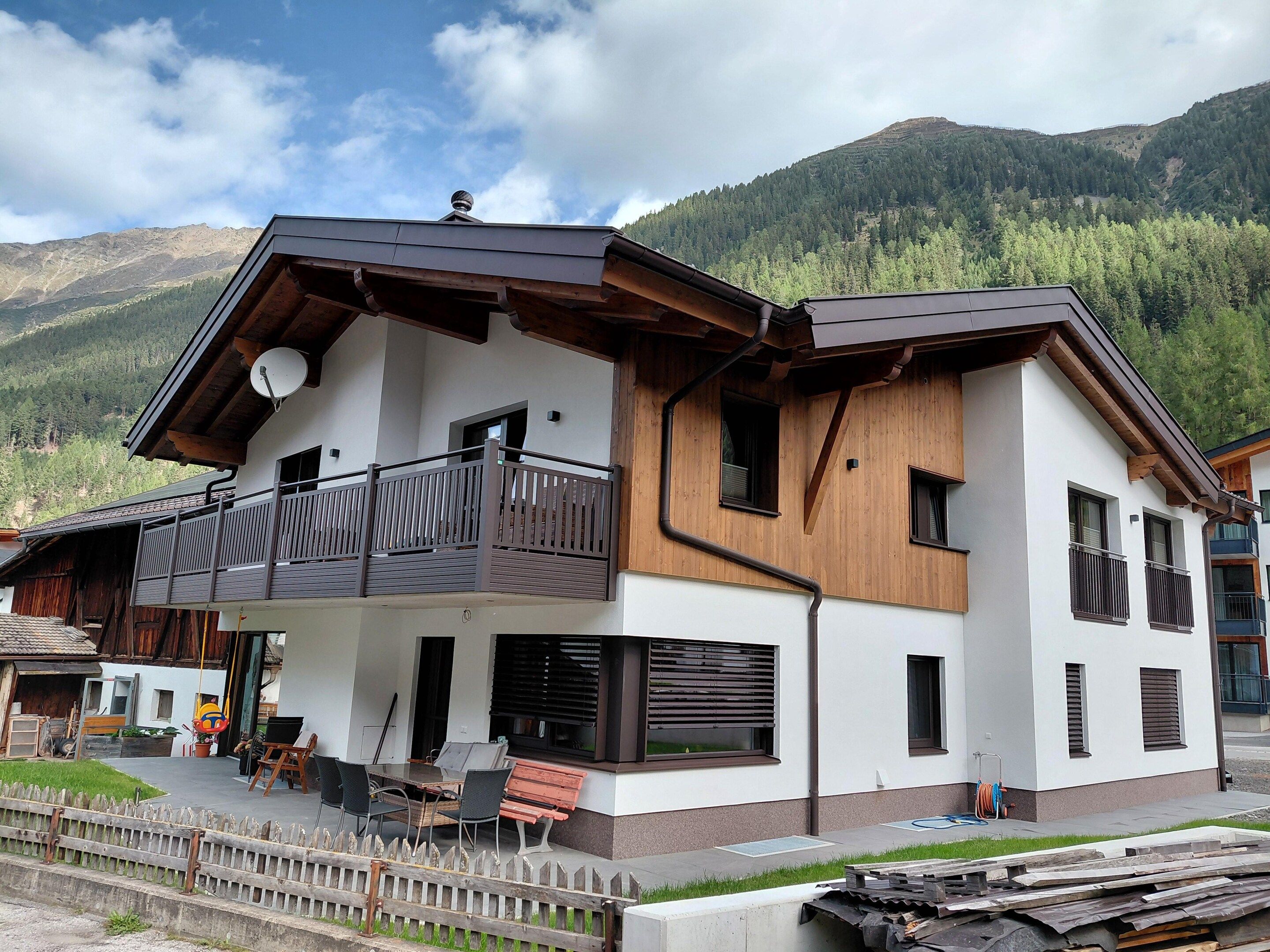 Un immeuble de deux étages doté d’un balcon, d’une antenne parabolique et offrant une vue sur une chaîne de montagnes boisée.