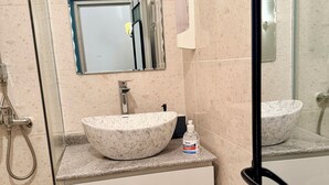 Un bagno con lavabo in marmo, uno specchio, un dispenser per sapone e una zona doccia.
