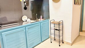 Una cucina con mobili blu, uno schienale nero, un lavello e un piccolo ripiano con una pianta e una bottiglia.