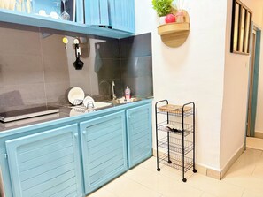 A kitchen with blue cabinets, a black backsplash, a sink, and a small shelf with a plant and a bottle. - Cozy studio apartment in Milan, in the heart of Bonapriso (Douala)