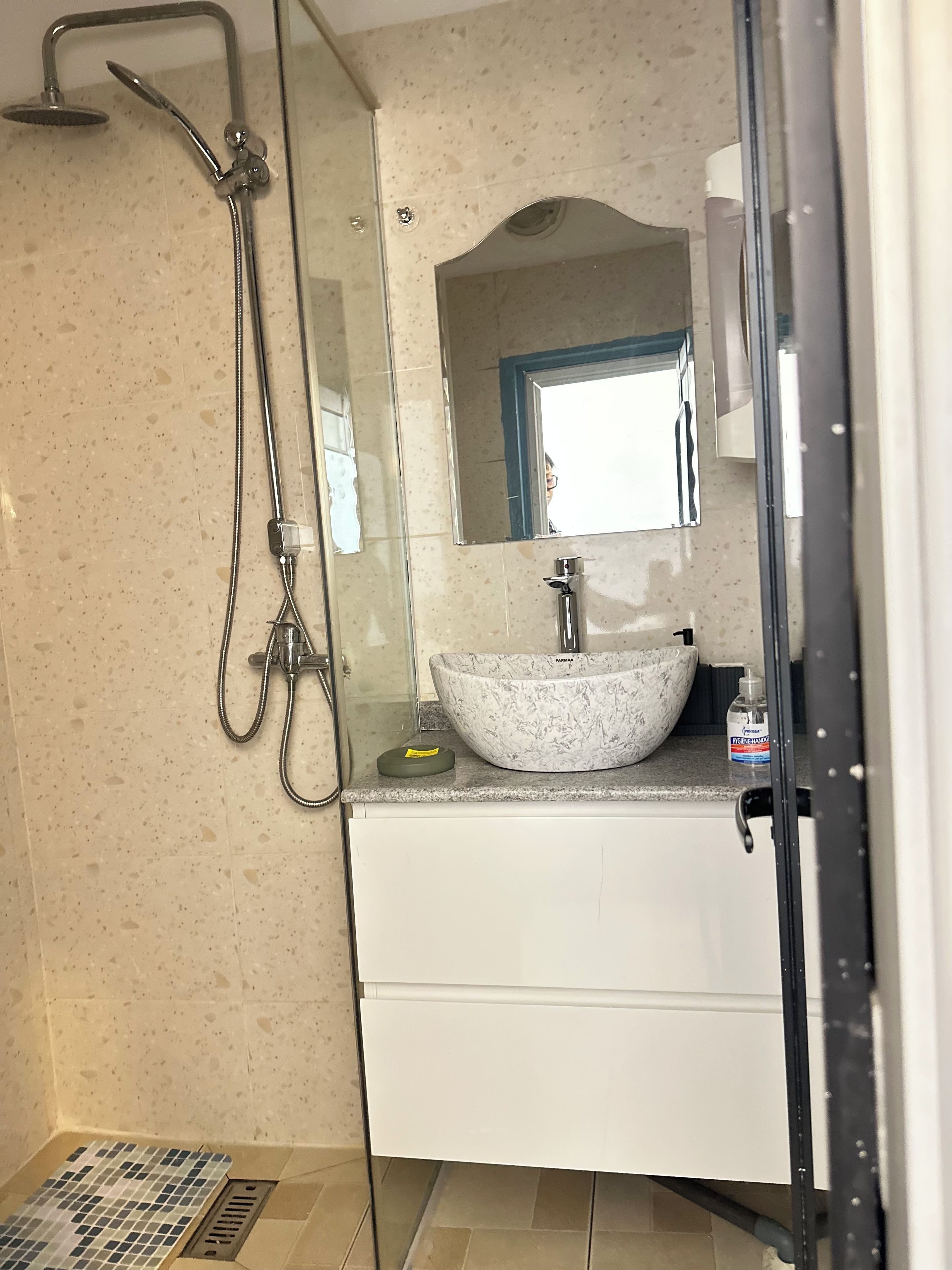Un baño con ducha envuelta en vidrio, lavamanos de mármol y espejo sobre el lavamanos.