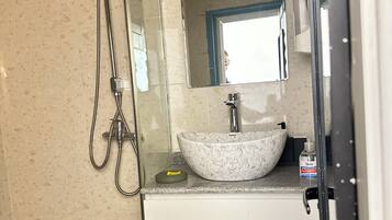 Un baño con ducha envuelta en vidrio, lavamanos de mármol y espejo sobre el lavamanos.