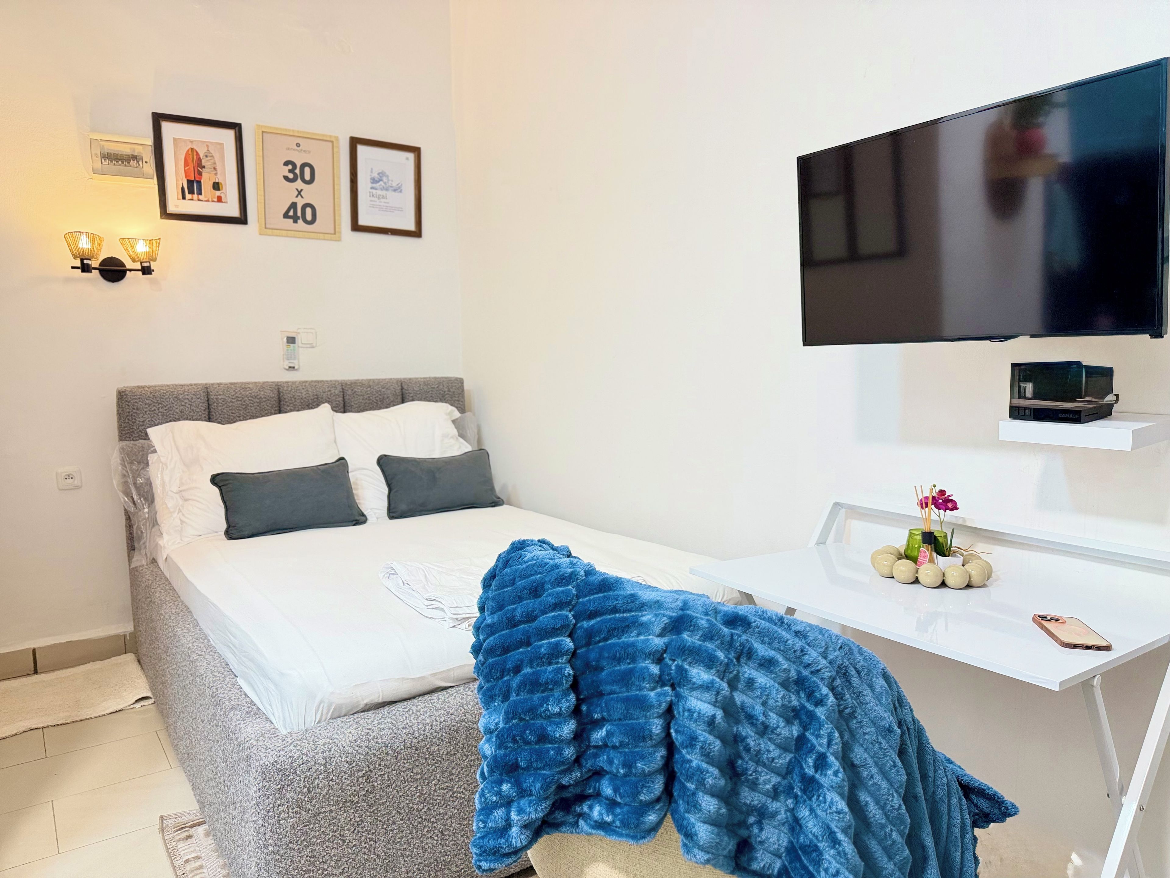 A bedroom with a bed, a TV, a desk, and a wall with framed pictures.