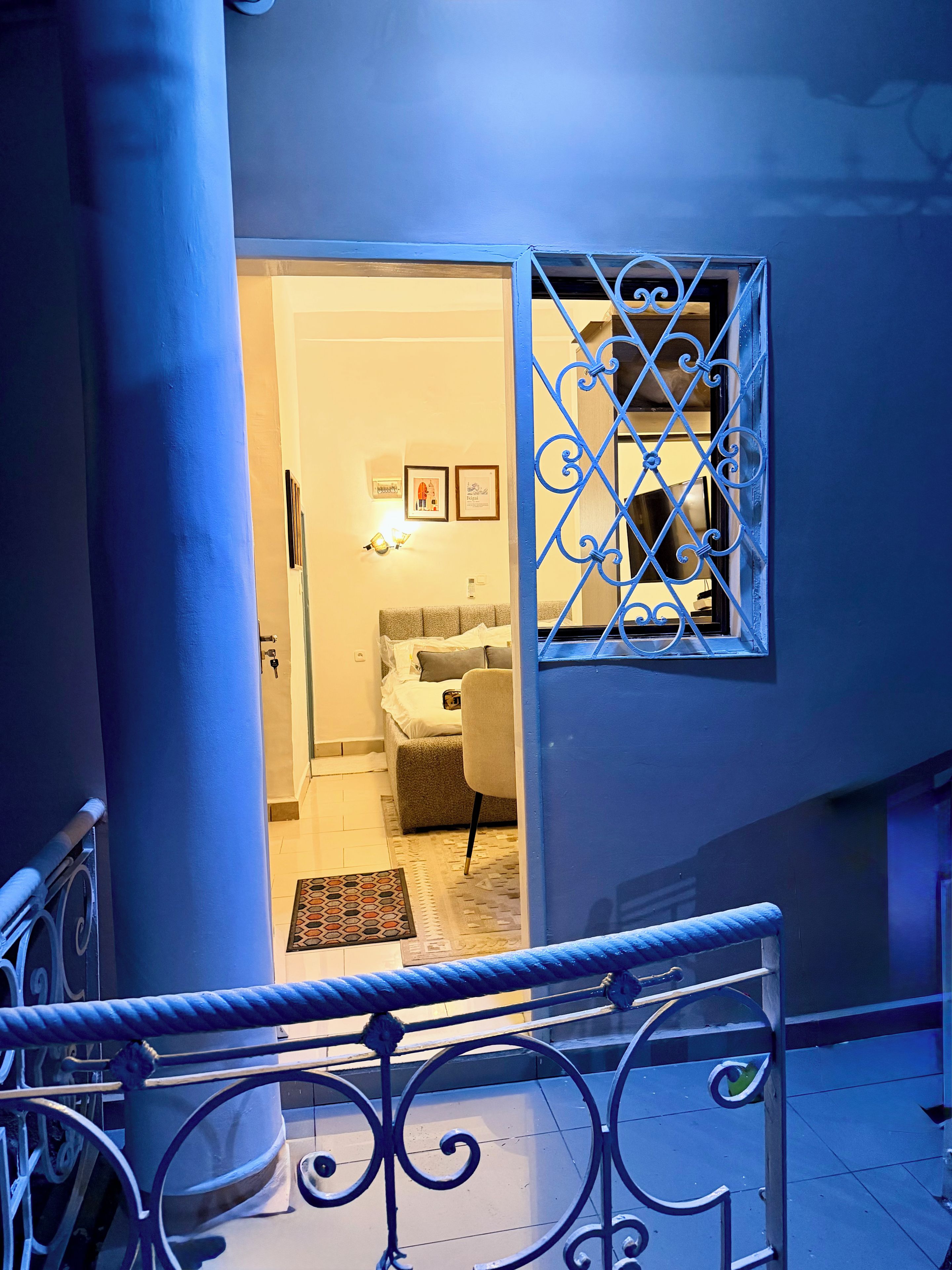 A staircase with a metal railing leading to a room with a bed, a chair, and a rug.