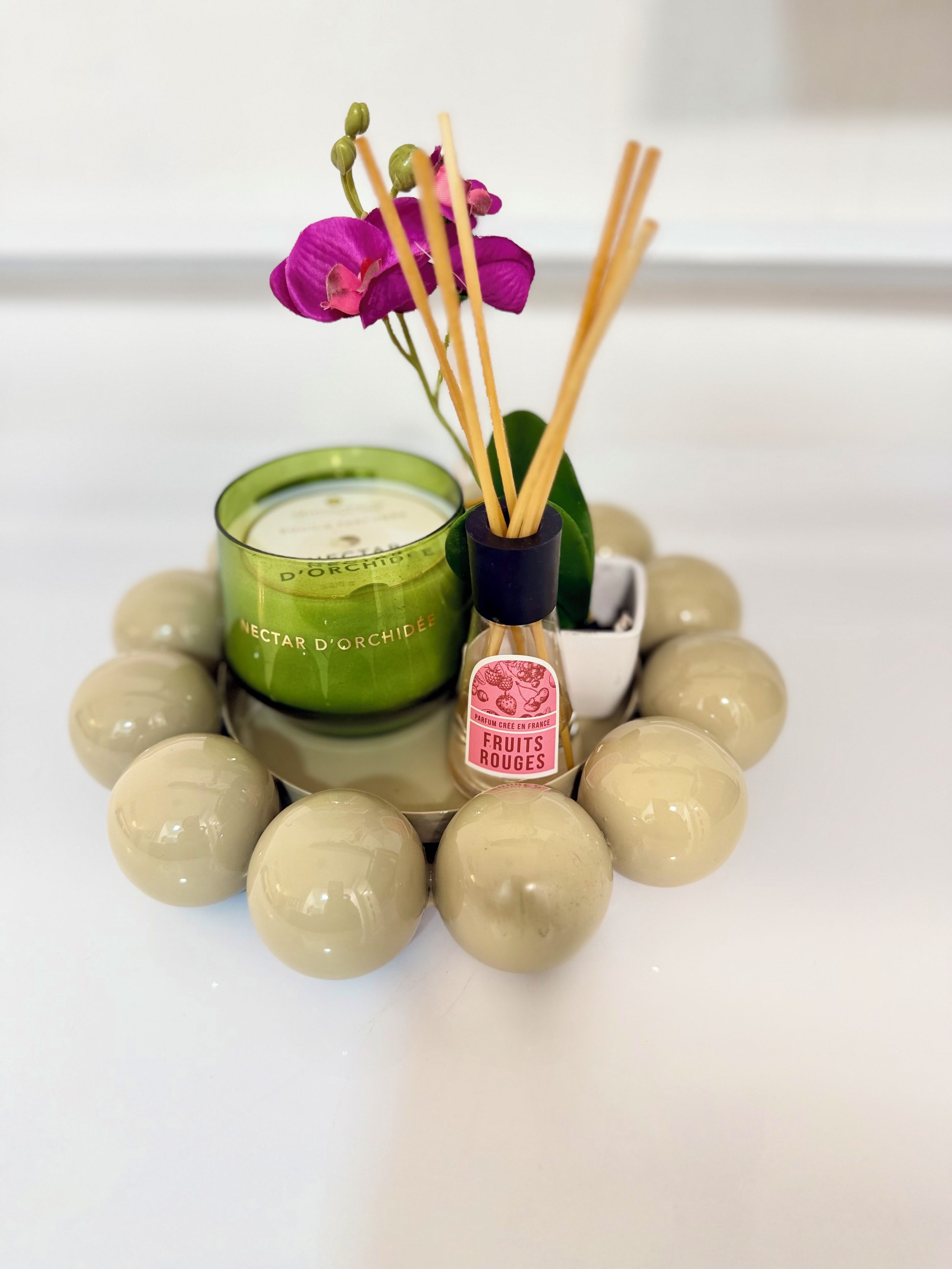 A green glass candle with a label, a small vase with a pink label and reed sticks, and several round objects.