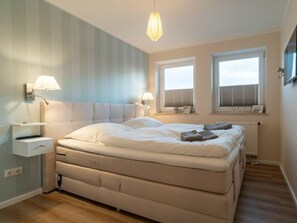 A bedroom with a bed, bedside tables, lamps, and windows. - Utholm 12 - Deichblick (St. Peter-Ording)