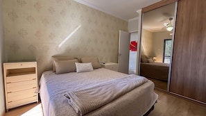 A bedroom with a bed, a wardrobe, a dresser, and a mirror. - SHB - 3 Suítes a 2 min praia (Guarujá)