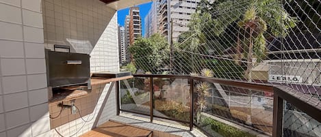 A balcony with a grill, tiled walls, and a view of a cityscape with high-rise buildings and greenery.