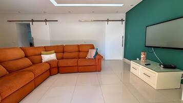 A modern living room with a sectional sofa, a flat-screen TV, and a minimalist cabinet.