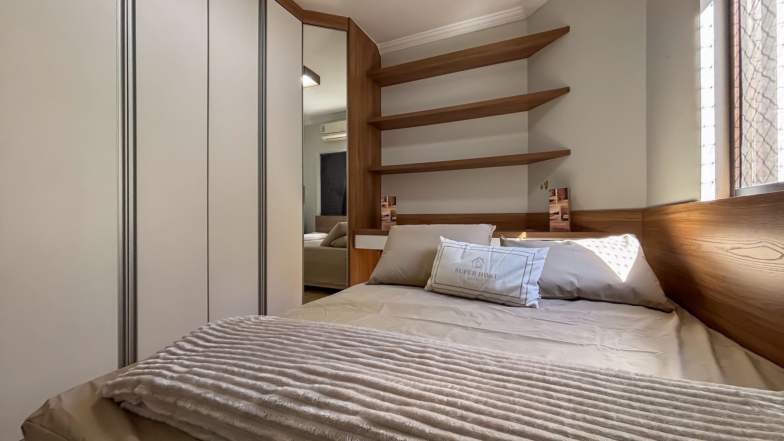 A bedroom with a bed, pillows, a bedside table, and a mirror.