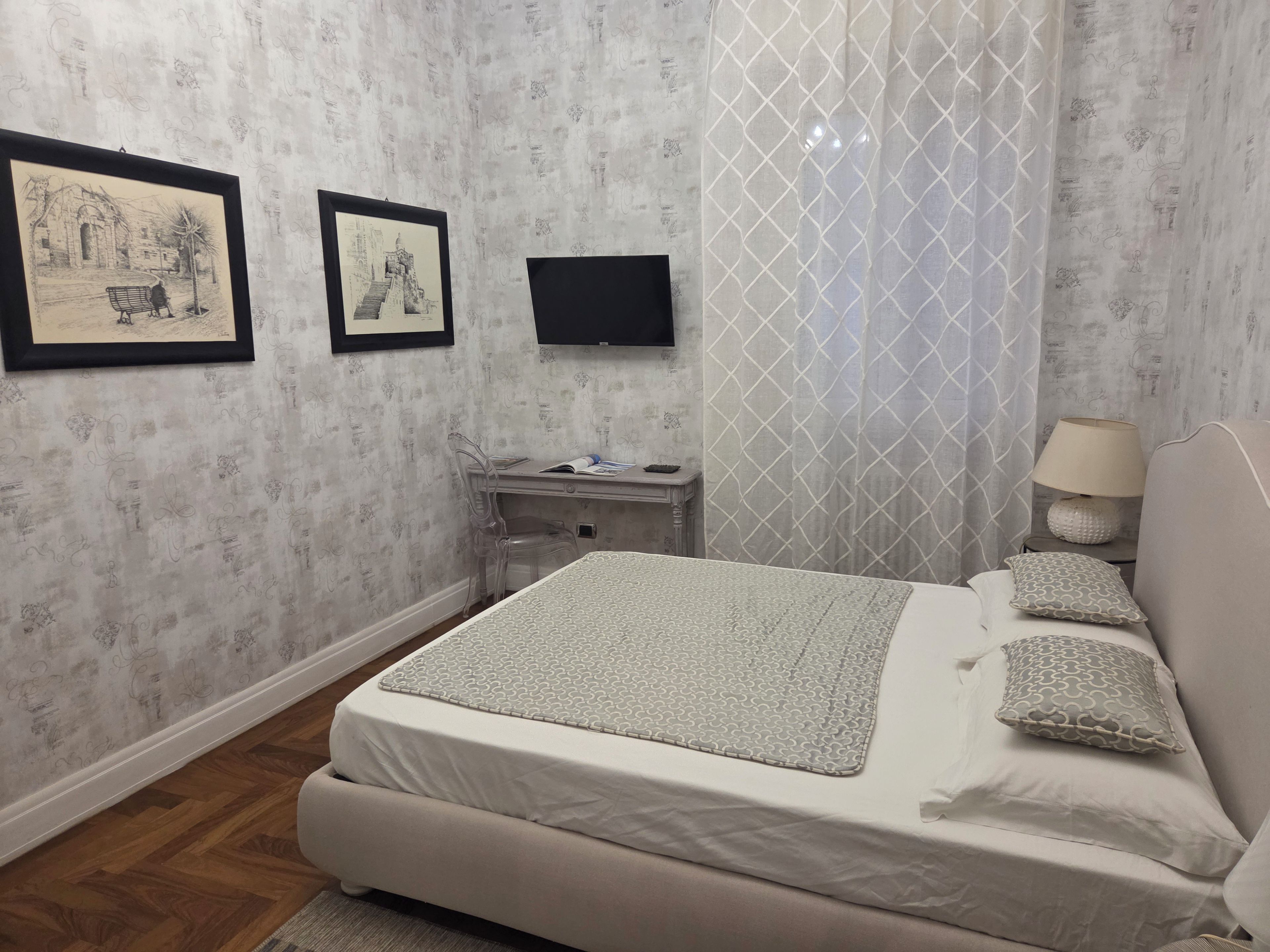 A bedroom with a bed, a desk, a chair, a TV, and two framed pictures on the wall.