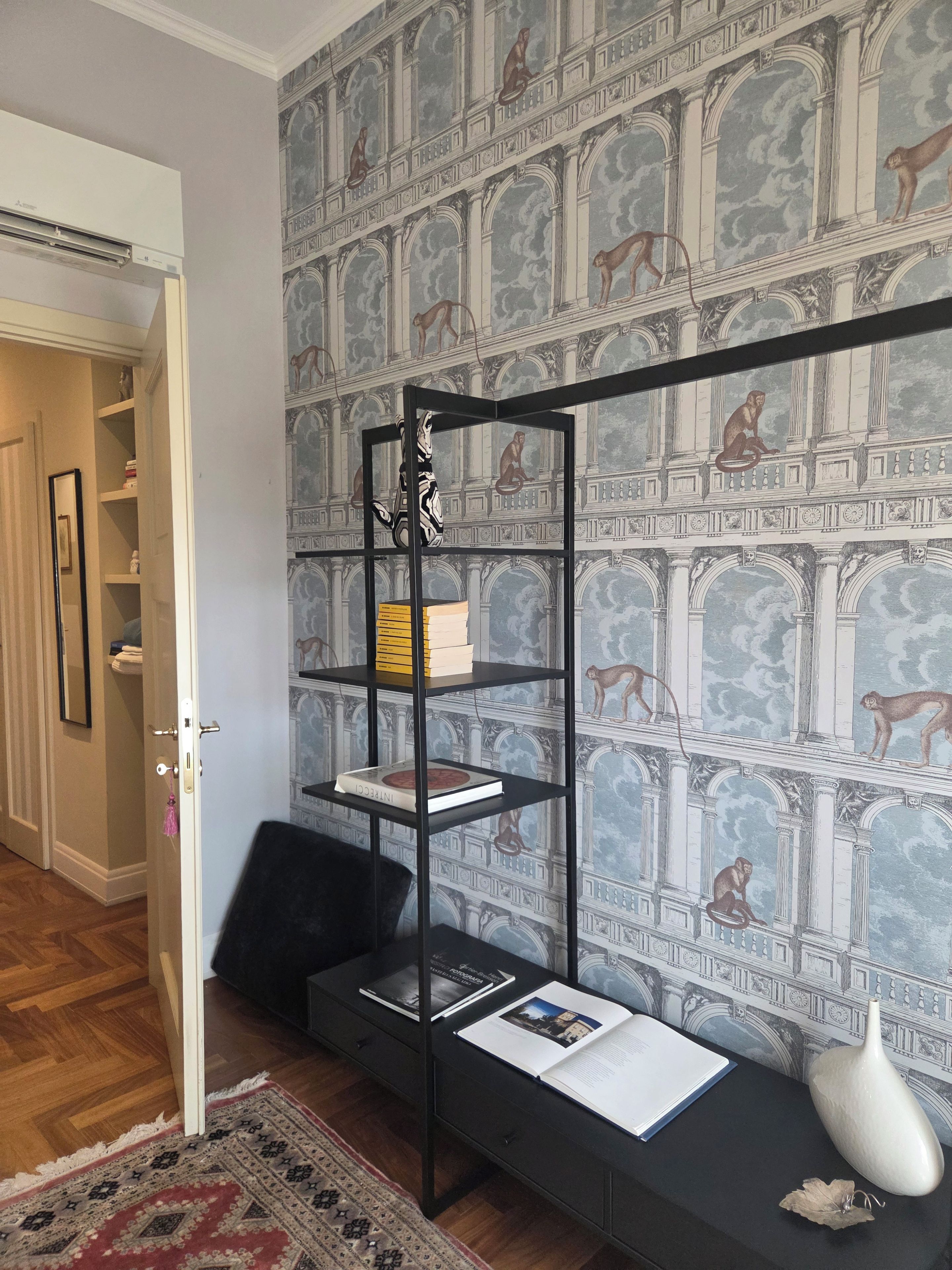 Quarto com uma estante de metal preto encostada a uma parede com um mural clássico.