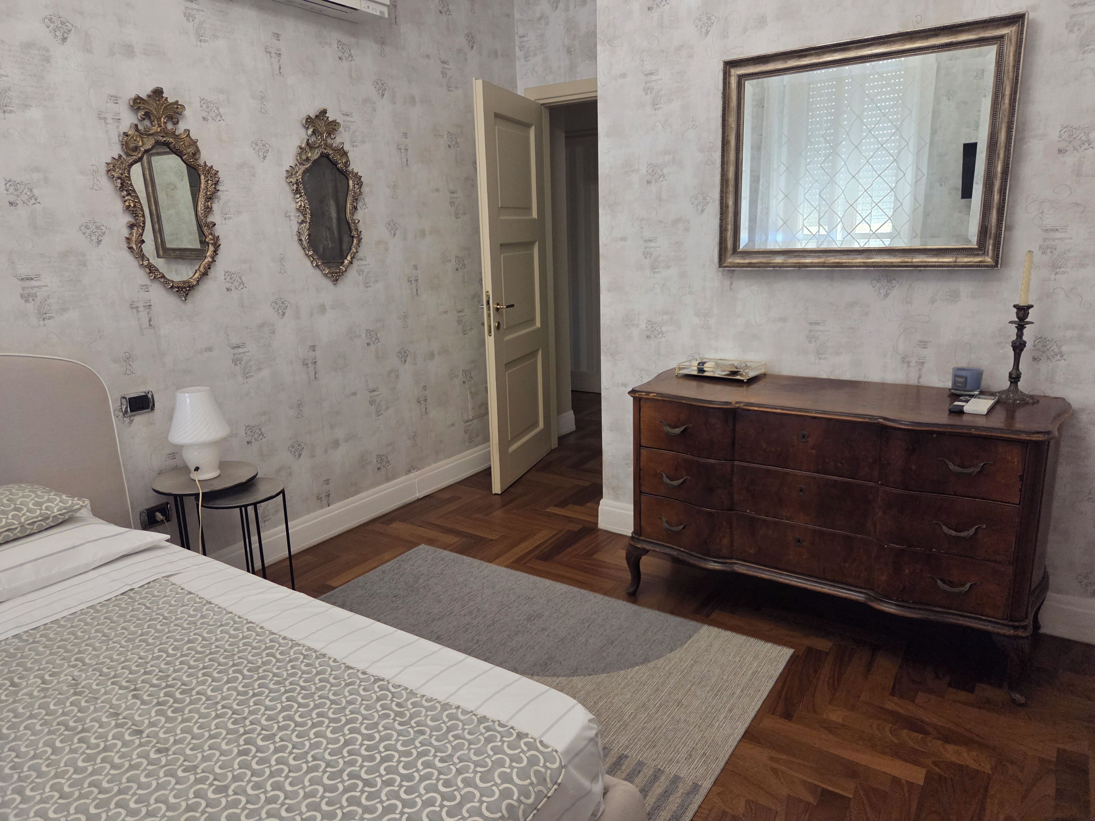 A bedroom with a bed, dresser, two wall mirrors, and a door leading to another room.