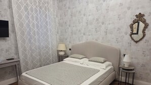 A neatly made bed with a patterned bedspread, a bedside lamp, and a decorative mirror on the wall. - STANZE CENTRO STORICO CAGLIARI (Cagliari)