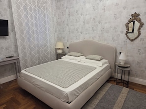 Una cama bien hecha con una colcha estampada, una lámpara de noche y un espejo decorativo en la pared.