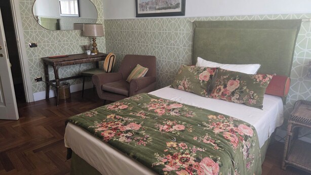 A bedroom with a bed, a chair, a desk, a mirror, and a framed picture on the wall. - STANZE CENTRO STORICO CAGLIARI (Cagliari)